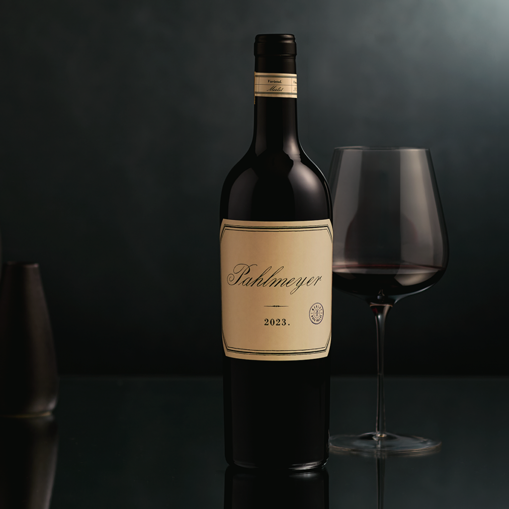 2023 Pahlmeyer Merlot bottle with glass of wine poured behind the bottle.